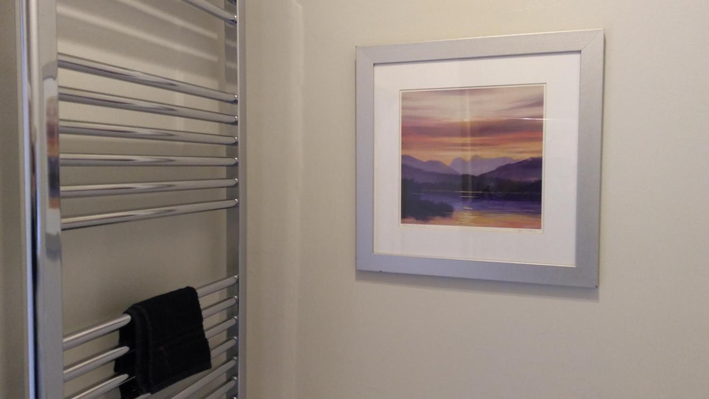 Ein Badezimmer mit Handtuchhalter und einem gerahmten Landschaftsbild an der Wand.