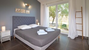 Un dormitorio moderno con una cama grande, una mesita de noche, una lámpara de pared y vistas al exterior.
