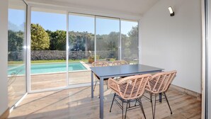 Una habitación moderna con puerta de vidrio que da a una piscina, una mesa con sillas y una pared de piedra al fondo.