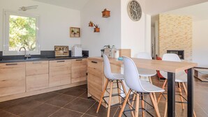 Una cocina moderna con armarios de madera, un lavamanos integrado y un comedor con mesa de madera y sillas blancas.