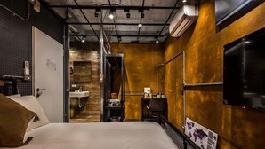 A hotel room with a bed, a desk, a chair, a TV, and a bathroom with a sink and mirror. - Reality Design Inn (Tainan)