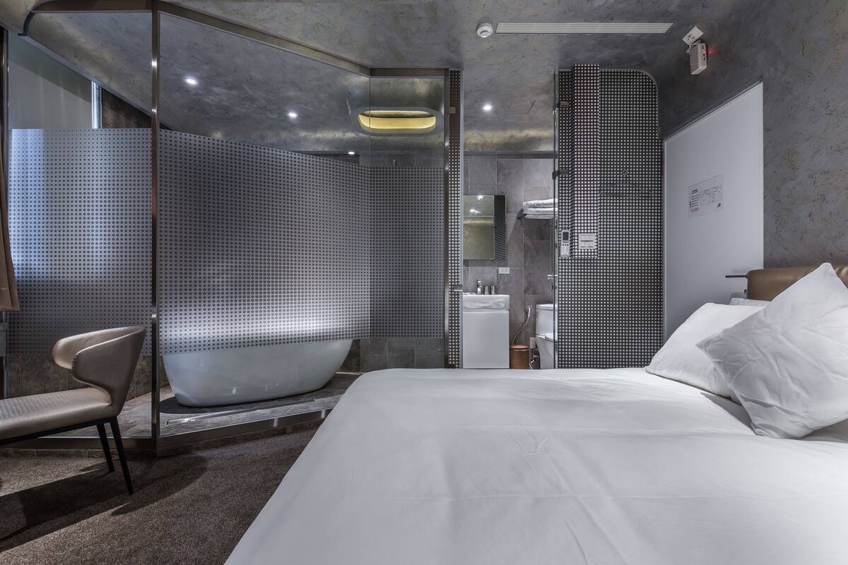 A modern hotel room with a large bed, a seating area, and a separate shower area.