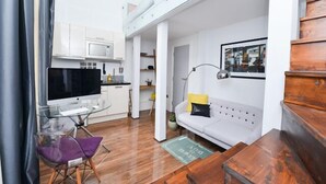 A compact living space with a kitchenette, a sofa, a dining table, and a TV.