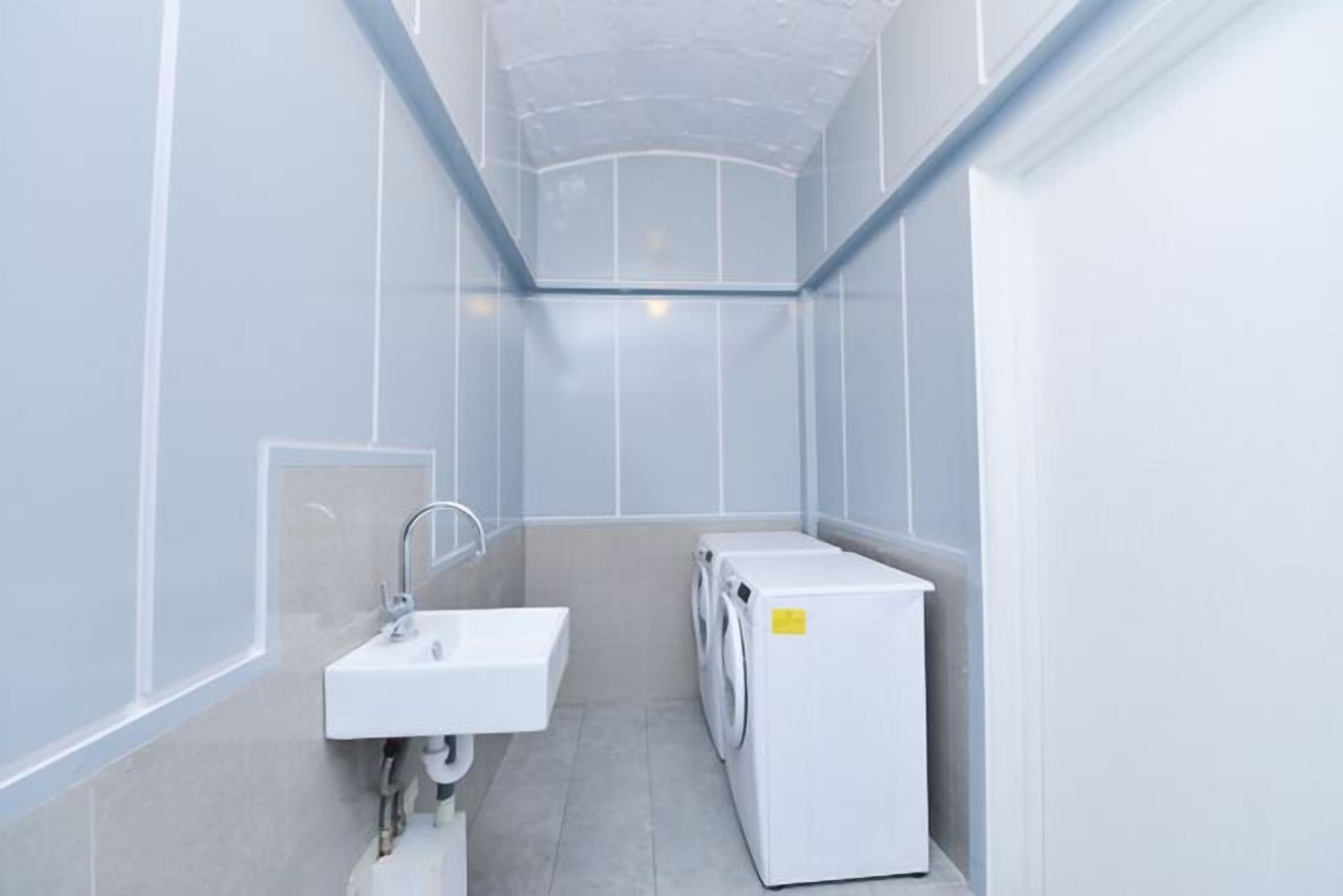 A compact, modern bathroom with a built-in sink, a washing machine, and a shower area.
