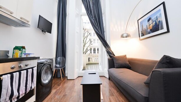 A compact living space with a sofa, a small table, a washing machine, and a television.