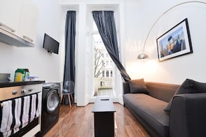 Un espace de vie compact comprenant un canapé, une petite table, un lave-linge et un téléviseur.
