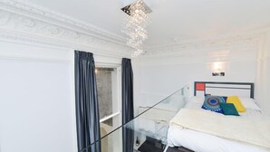 A hotel room with a bed, a glass partition, a chandelier, and a view of the outside.