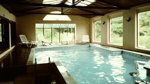 Una piscina interior con agua cristalina, rodeada de ventanas y sillas blancas.