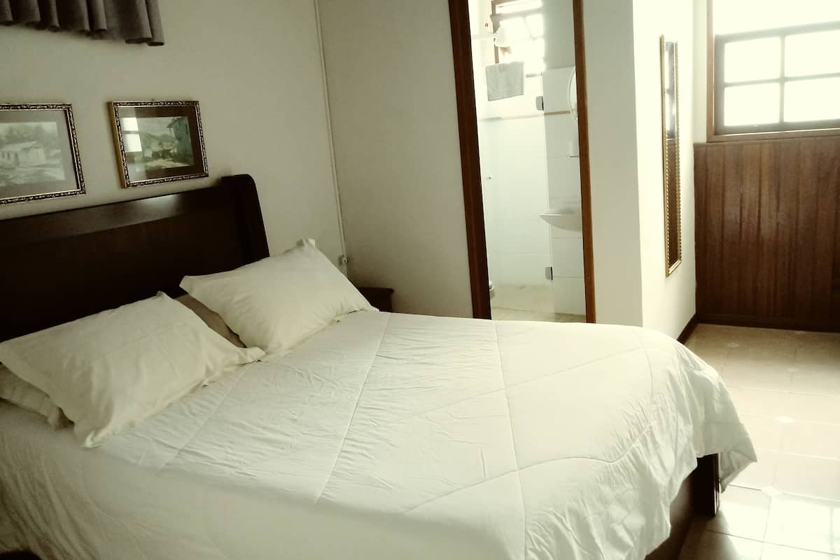 A neatly made bed with white linens in a room with a wooden headboard.