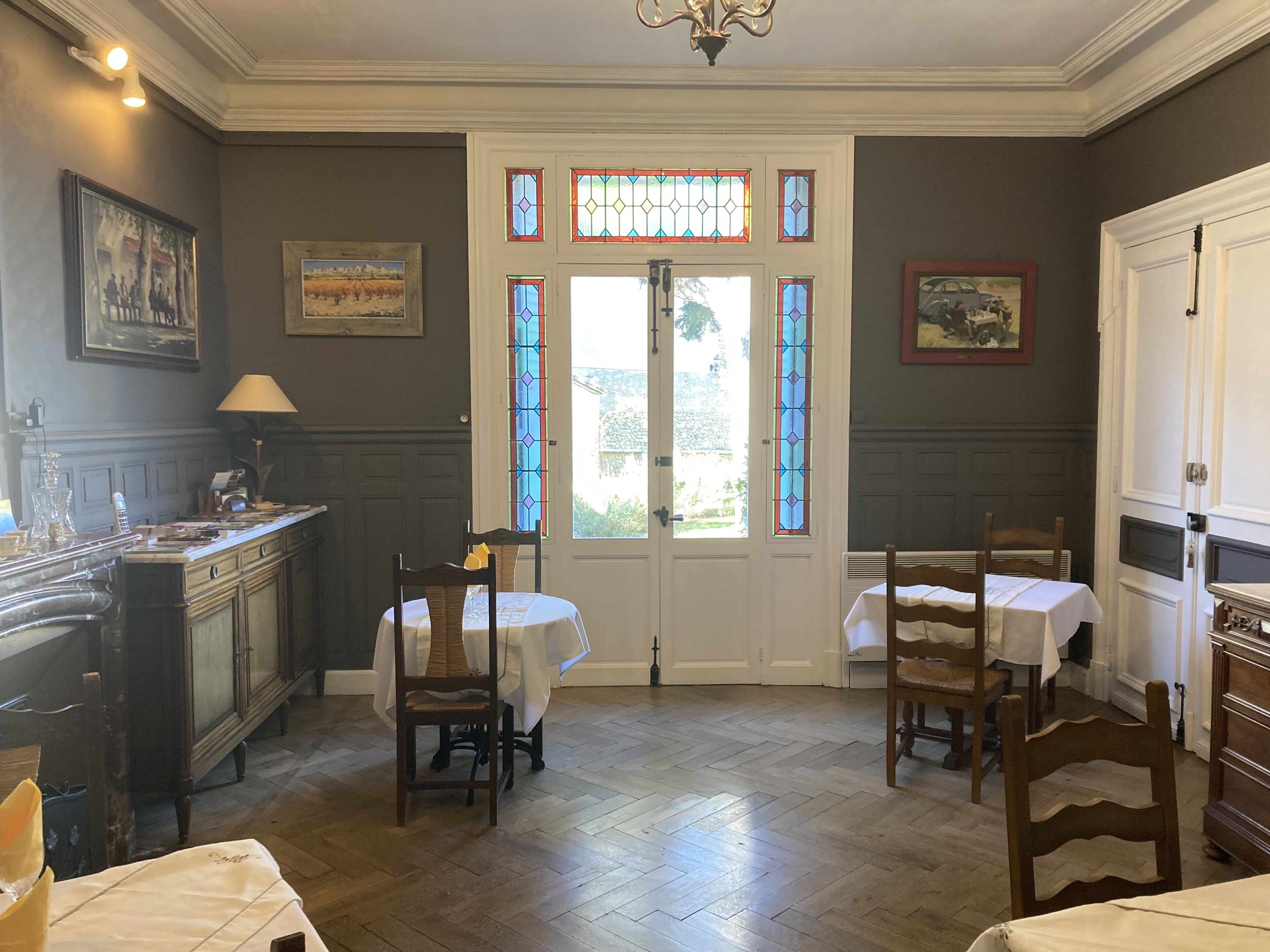 Una habitación con piso de madera, una puerta blanca con vidrieras y dos mesas con manteles blancos.