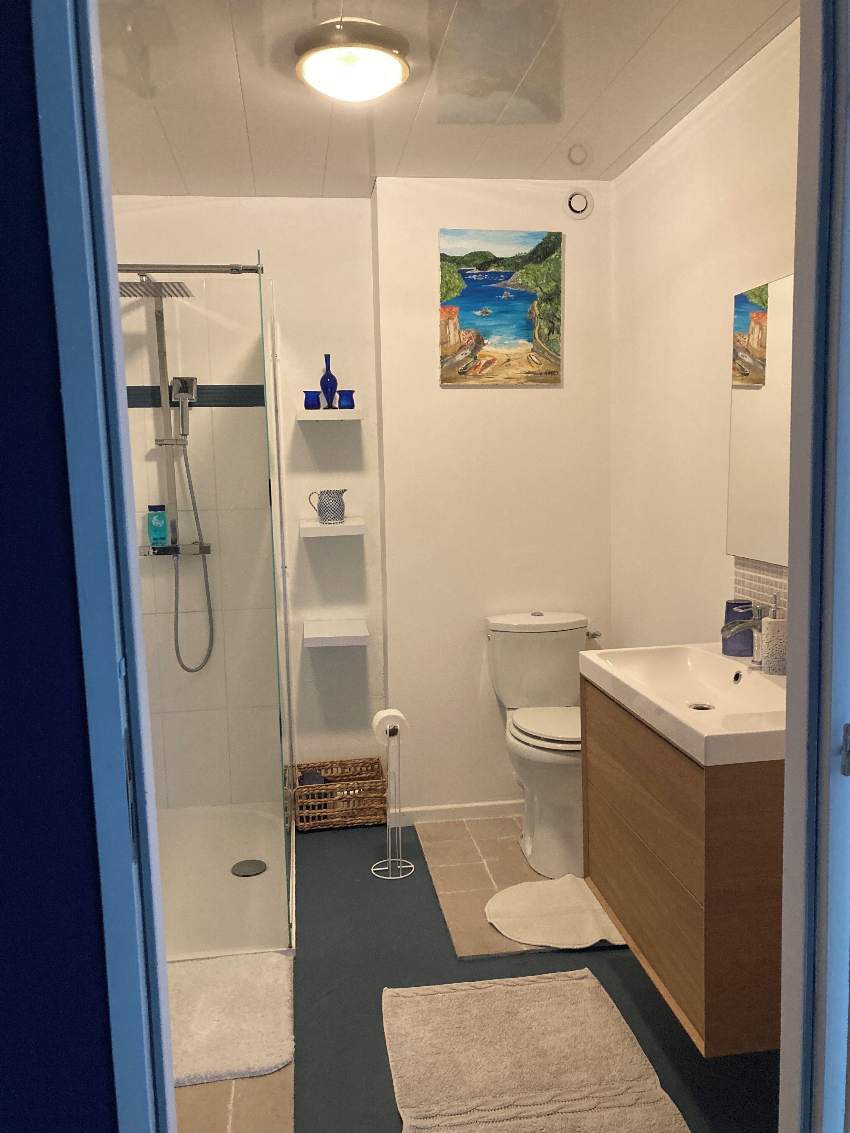 A bathroom with a shower, toilet, sink, and a painting on the wall.