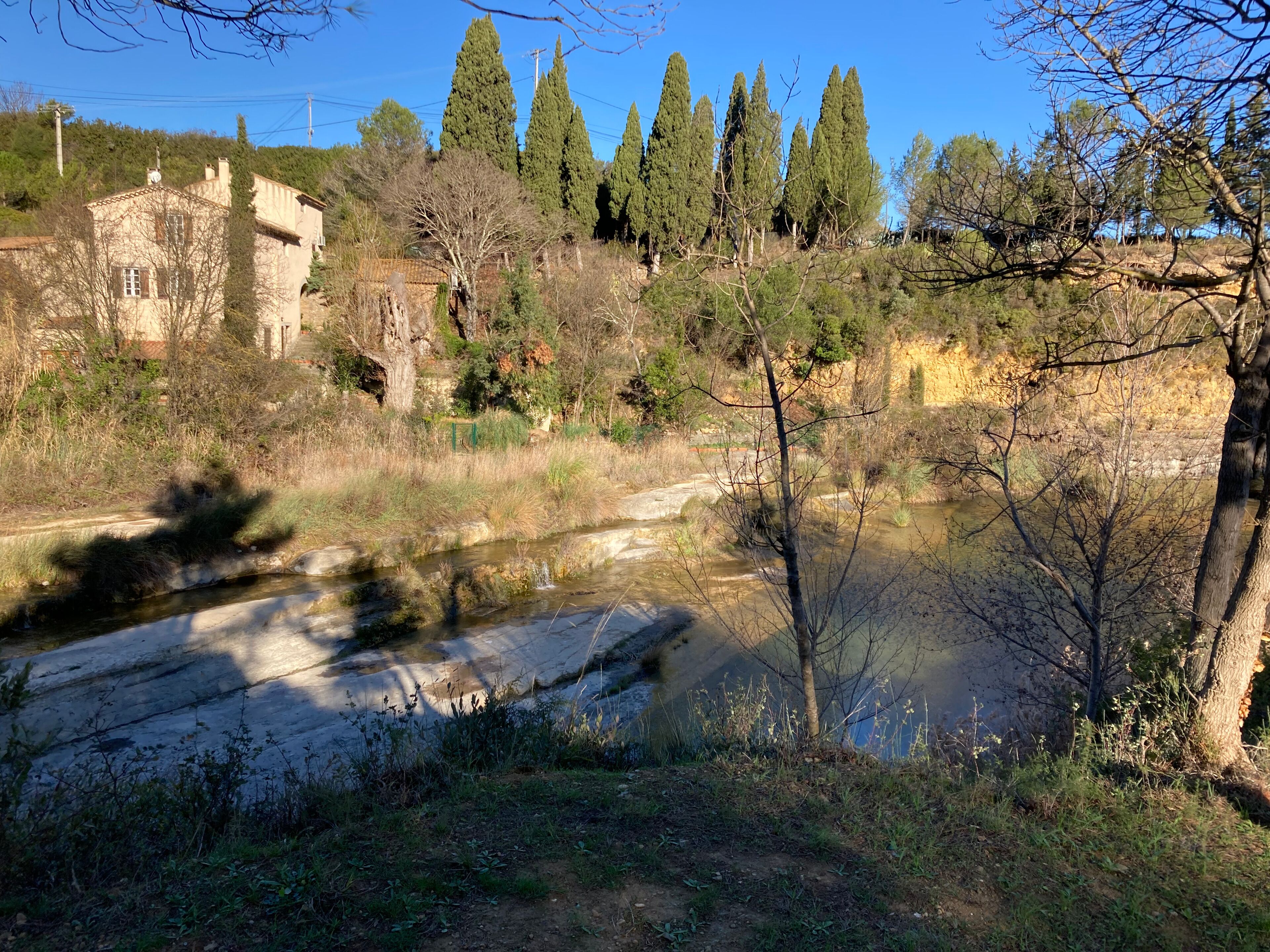 A rural landscape with a small stream, trees, and a building with a tiled roof.
