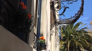 A building with ornate wrought iron balcony railings, potted orange flowers, and a palm tree in the background. - Villa Celine (Saint-Laurent-de-la-Cabrerisse)