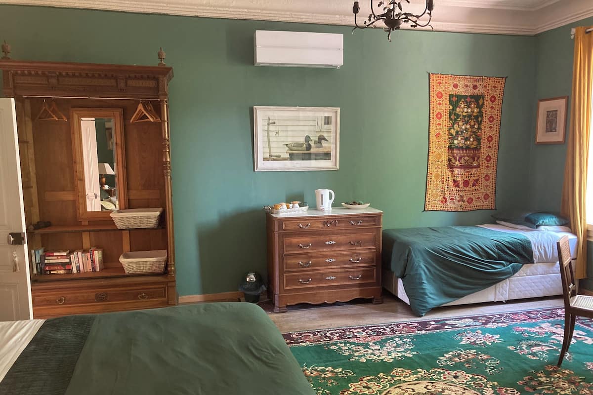 A room with a bed, a dresser, a mirror, a tapestry, and a framed picture on the wall.