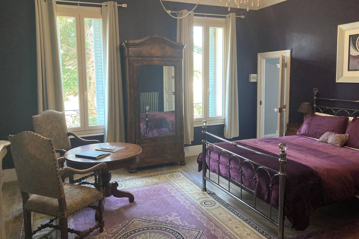 A bedroom with a bed, a chair, a table, a mirror, and a chandelier.