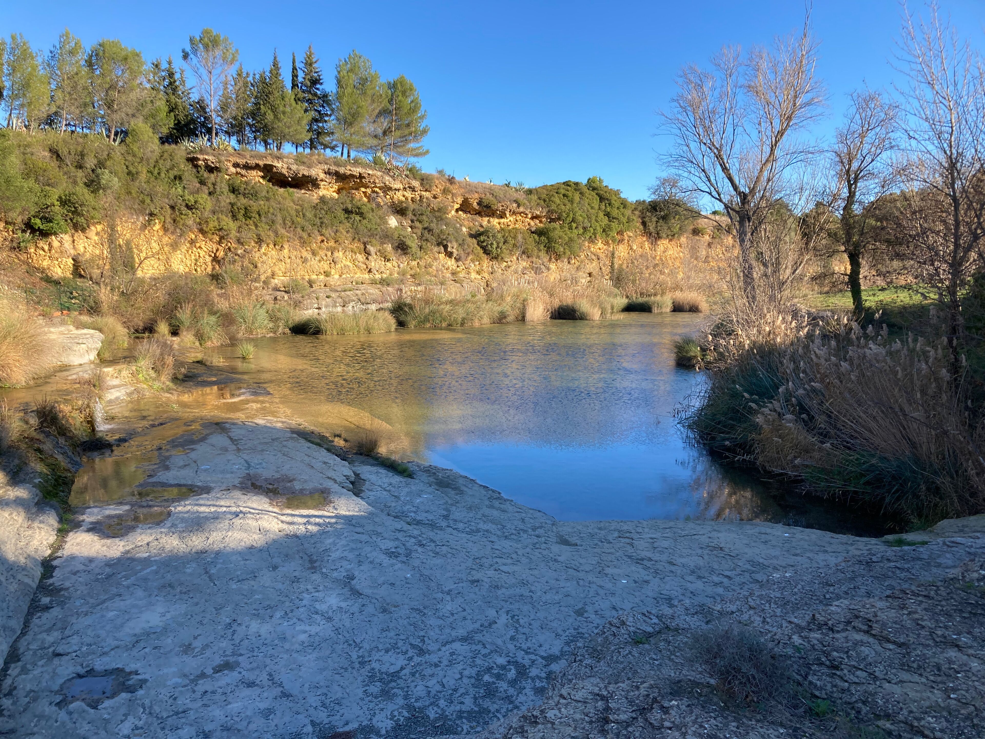 A natural landscape with a calm river, rocky terrain, and sparse vegetation.