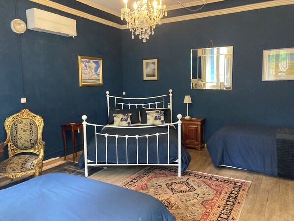A bedroom with a white metal bed frame, two blue beds, a chandelier, and a patterned rug.