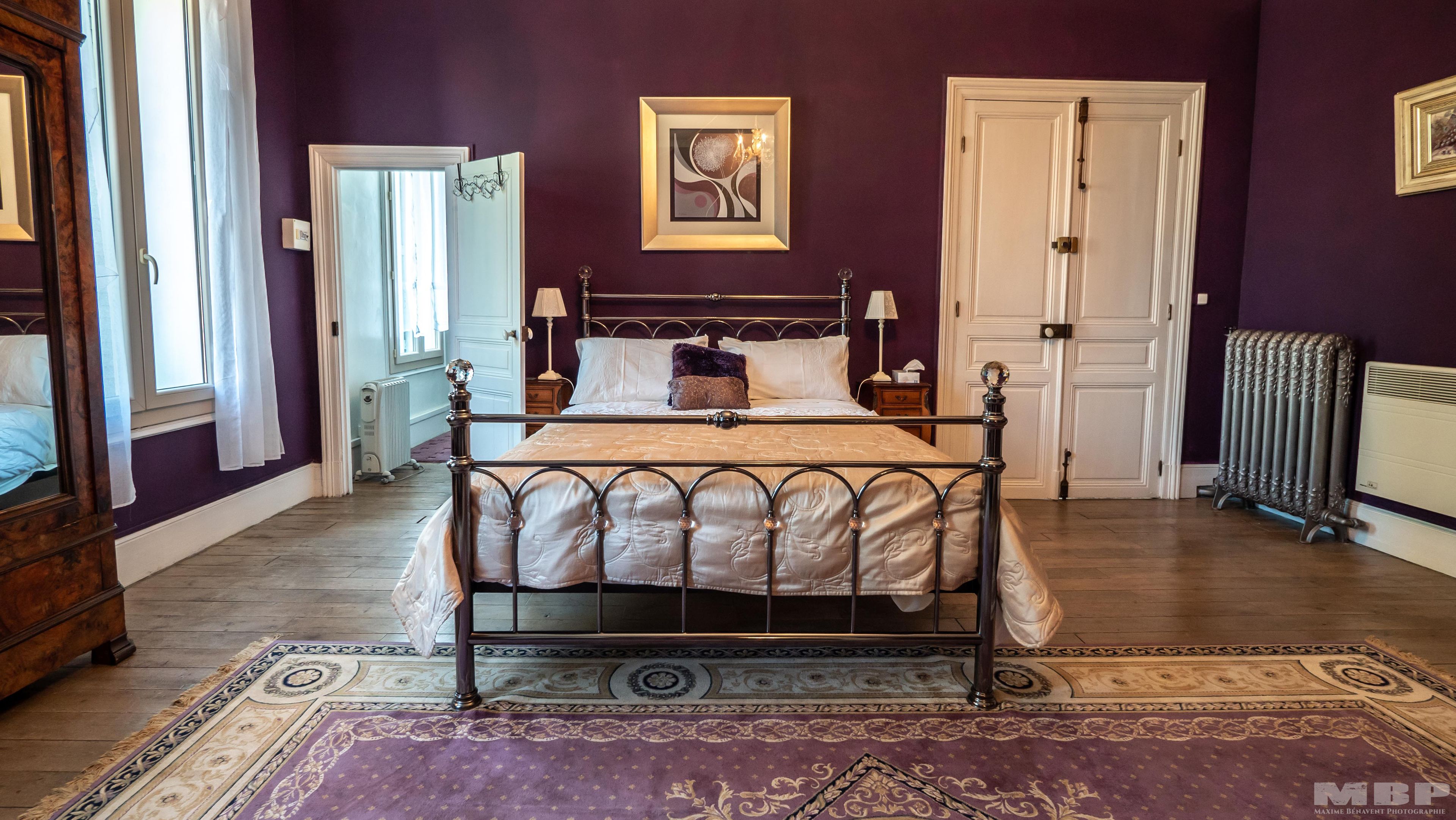 A bedroom with a four-poster bed, a radiator, a door, and a window with curtains.