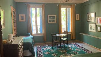 A room with a bed, a desk with a chair, a chandelier, and a large window with curtains.