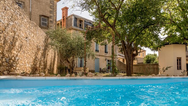 A swimming pool with clear blue water, surrounded by stone walls and trees. - Villa Celine (Saint-Laurent-de-la-Cabrerisse)