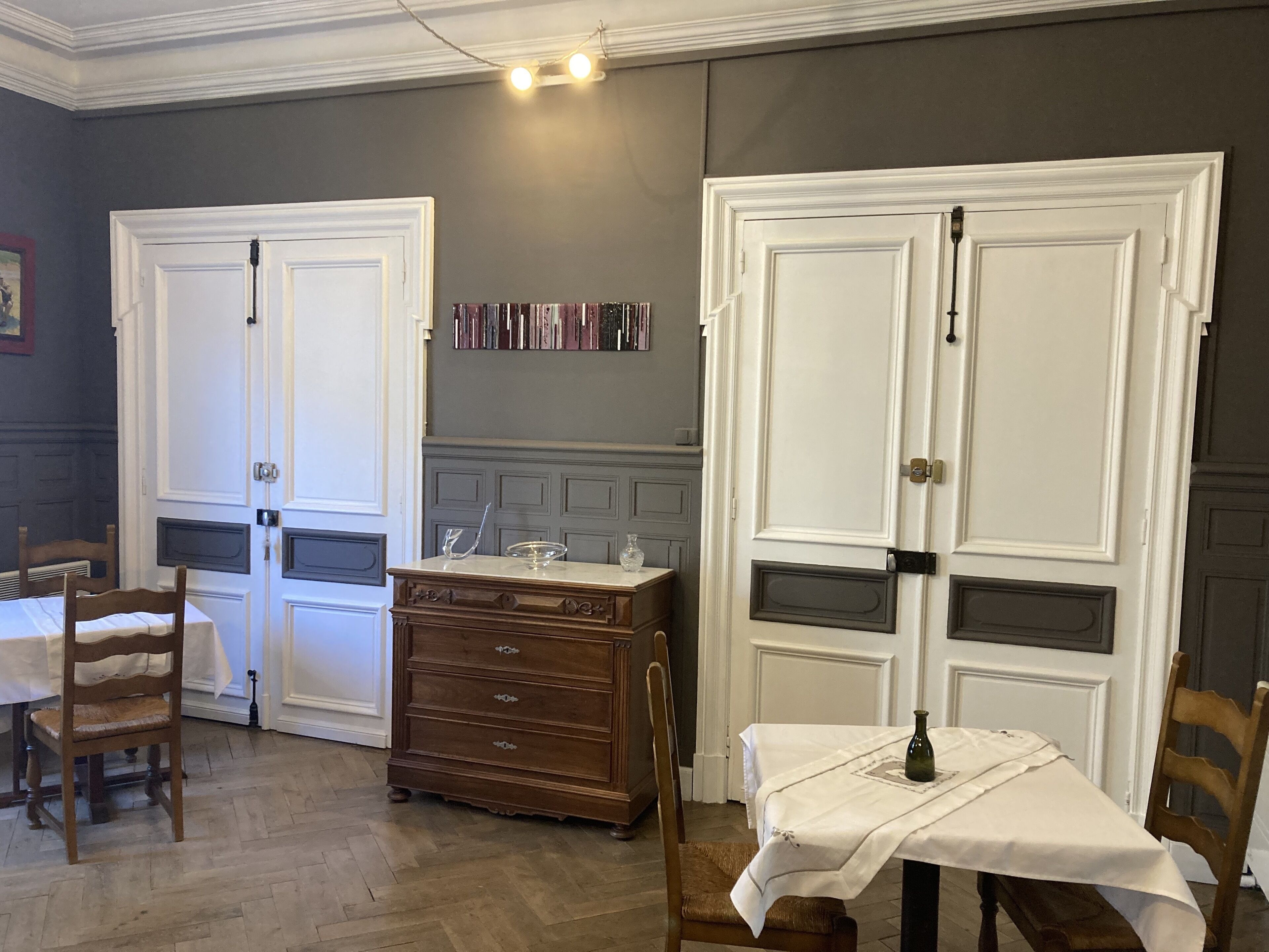 Een kamer met twee witte deuren, een houten dressoir, een tafel met een witte tafelkleed, en een stoel.
