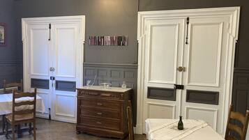Een kamer met twee witte deuren, een houten dressoir, een tafel met een witte tafelkleed, en een stoel.