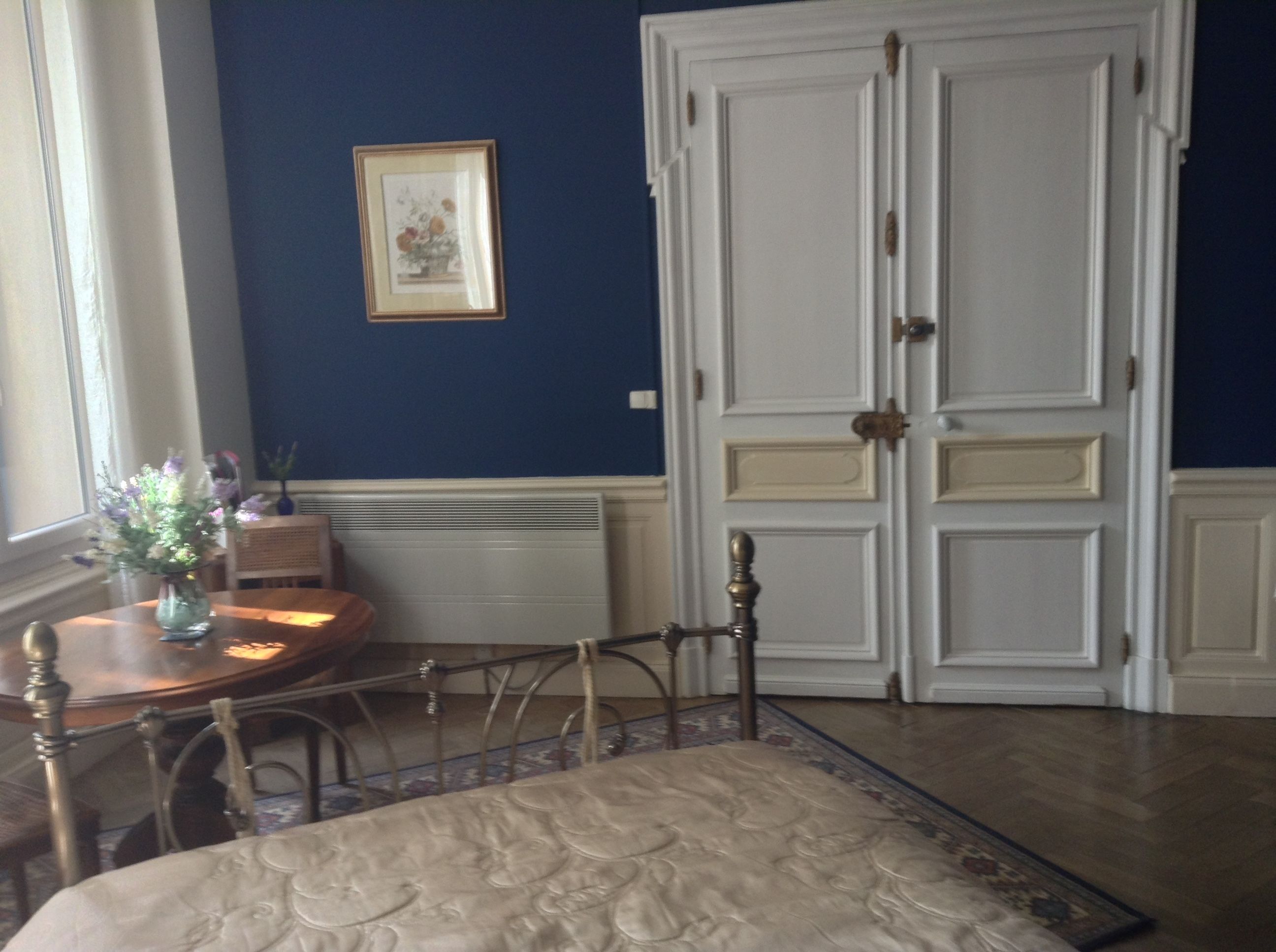 Una stanza con un'ampia porta bianca a due ante, un quadro appeso al muro, un tavolo rotondo in legno con un vaso di fiori e un tappeto decorato sul pavimento.