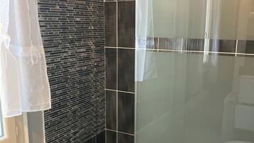 Een moderne badkamer met een douchecabine van glas, een zwart-wit betegelde muur en een zichtbare toiletrolhouder.