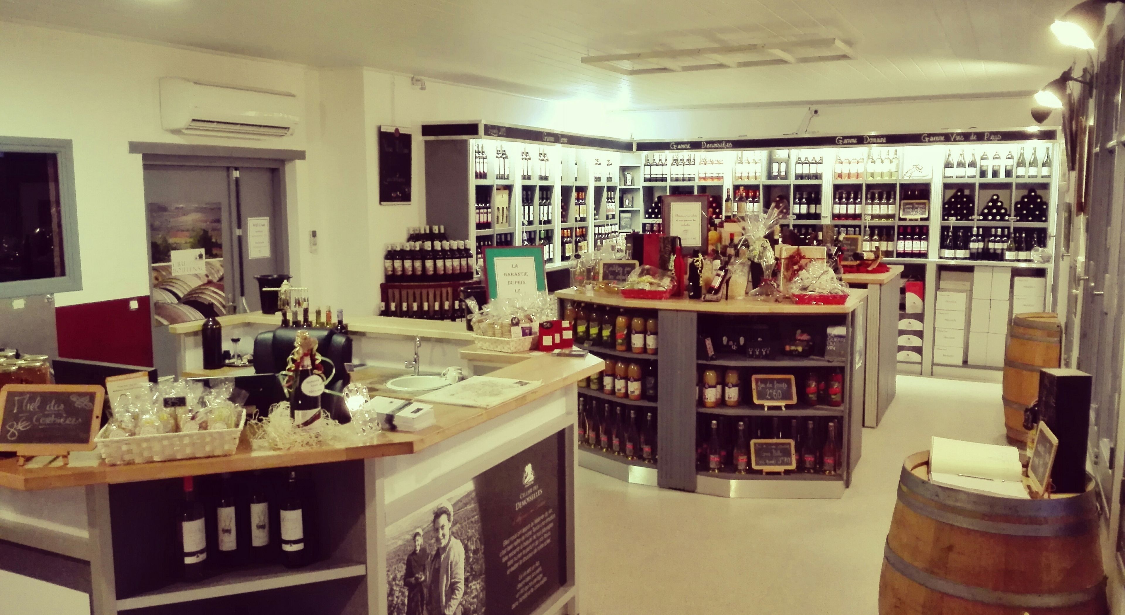 Una tienda de vinos con estantes llenos de botellas, una barra con copas de vino y un barril.