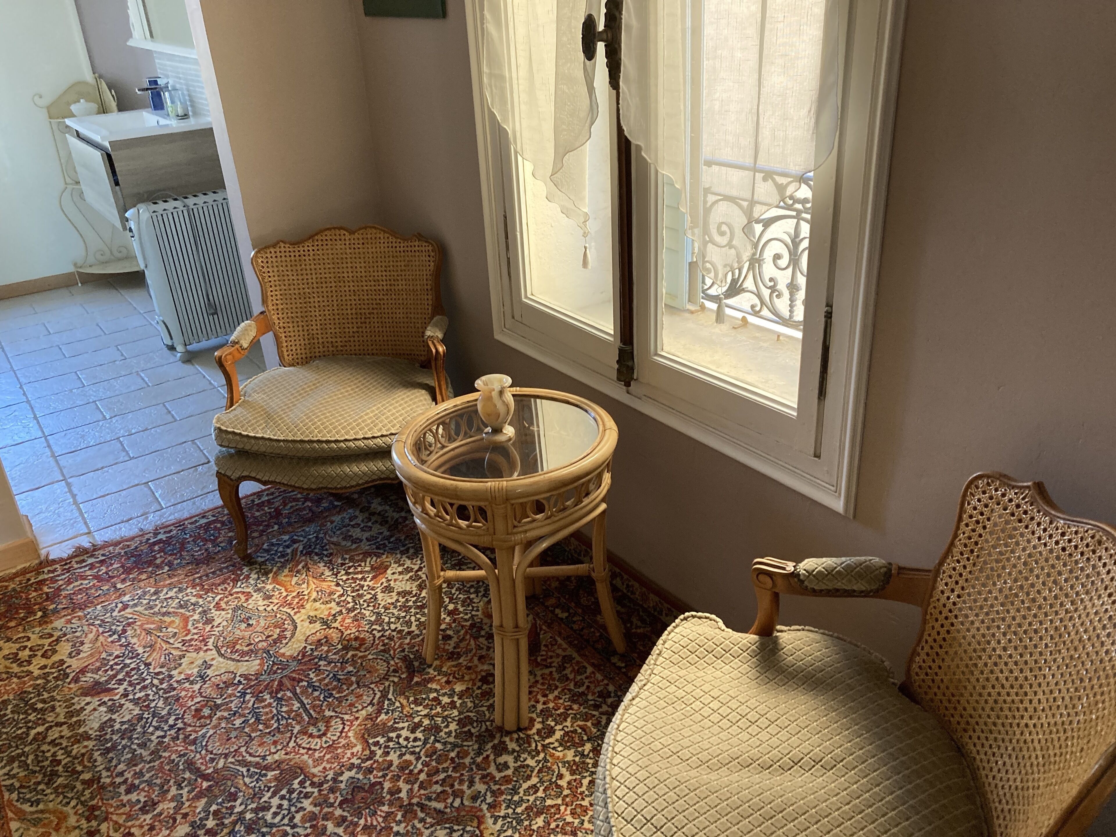 A room with two wicker chairs, a small round table, and a patterned carpet.
