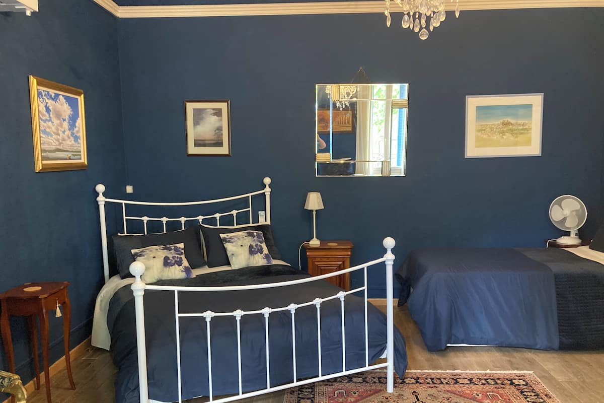 A bedroom with a white metal bed frame, a blue wall, a chandelier, a mirror, and a rug.