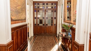 A grand hallway with a marble floor, wooden doors with intricate designs, and a large mirror on the right. - Villa Celine (Saint-Laurent-de-la-Cabrerisse)