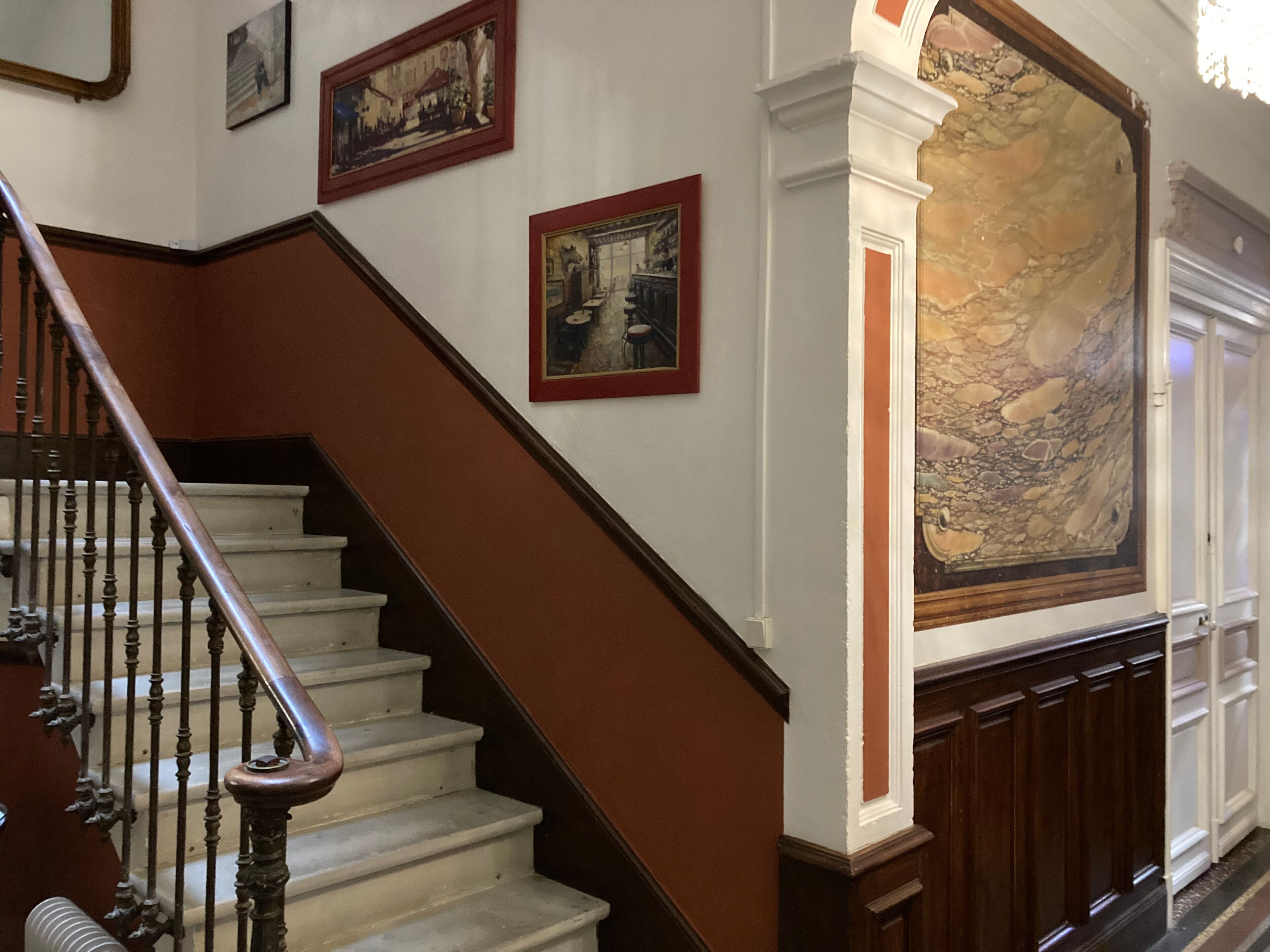 A staircase with wooden balusters and a marble wall with a large painting.