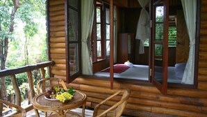 A wooden cabin with a balcony, wicker furniture, and a bed with a red pillow. - Banhalawee (Ko Yao)
