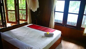 A wooden bed with a white mattress and red placemat, large windows with curtains, and a wooden floor. - Banhalawee (Ko Yao)