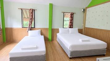 A hotel room with two beds, wooden flooring, a green accent wall, and a window with curtains.