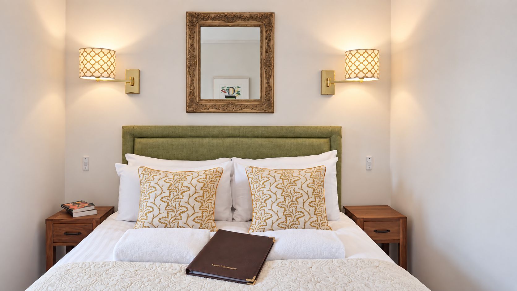 A neatly made bed with a green headboard, two bedside tables with lamps, and a framed picture on the wall.