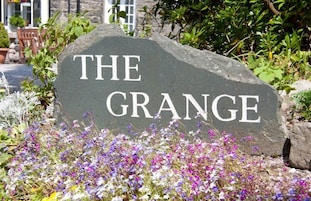 Un letrero de piedra con el texto “THE GRANGE” rodeado de diversas flores.