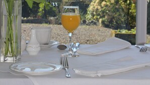 Una mesa dispuesta con un vaso de jugo de naranja, un florero y vistas a las montañas a través de una ventana.