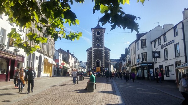 A historic town square with cobblestone streets, a prominent clock tower, and various commercial buildings including a pub and a hotel. - The Grange Country House (Keswick)