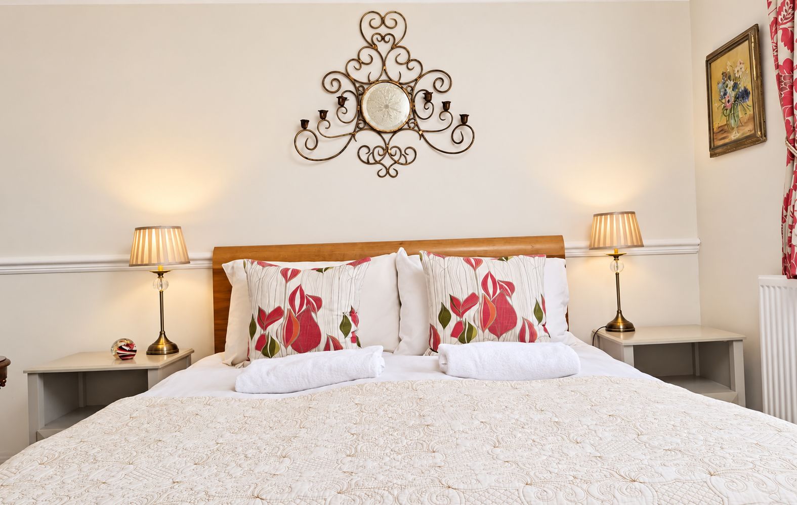 A neatly made bed with a floral-patterned pillow, a decorative wall piece above it, and two bedside lamps on nightstands.