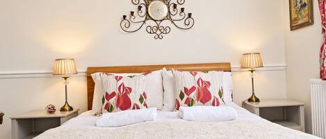 A neatly made bed with a floral-patterned pillow, a decorative wall piece above it, and two bedside lamps on nightstands.