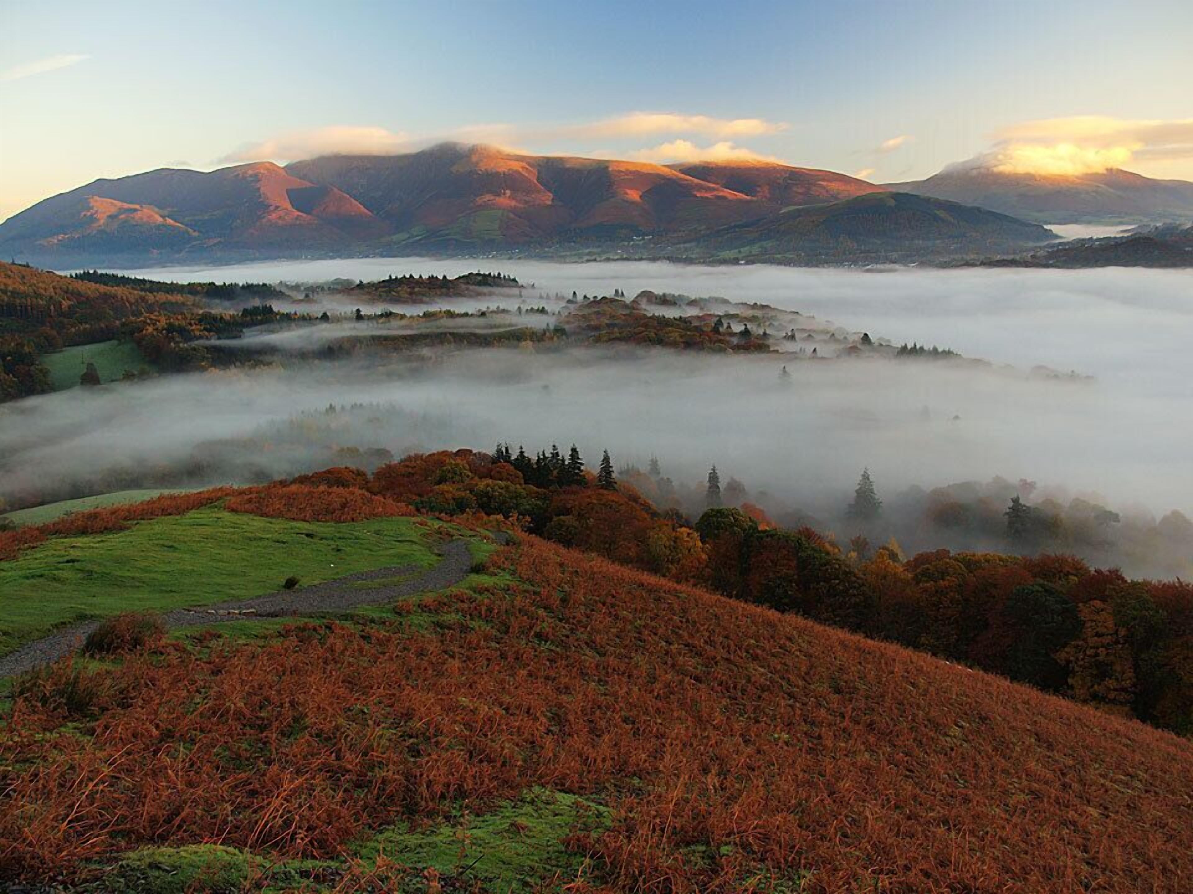 A mountainous landscape with a valley shrouded in mist, surrounded by autumn-colored trees.