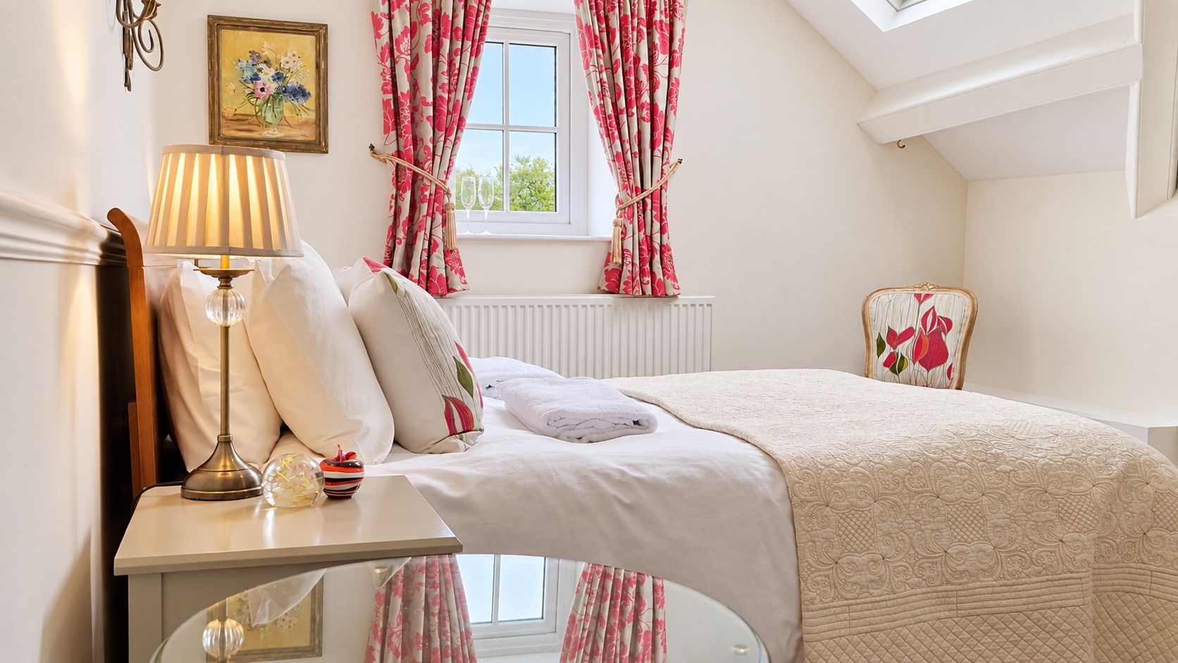 A bedroom with a bed, bedside table, lamp, and floral curtains.
