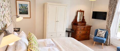 Un dormitorio con cama, cómoda, silla, televisor y ventana con cortinas.