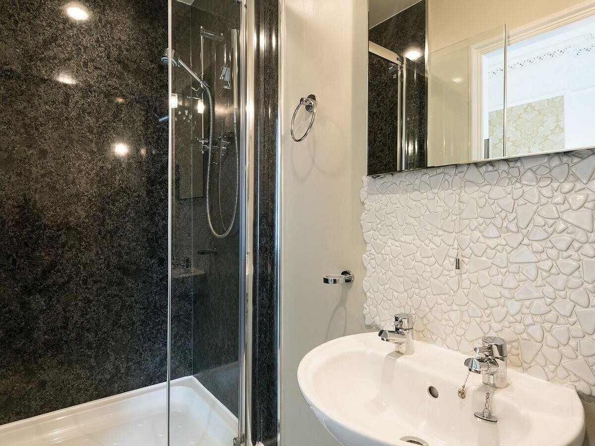 A modern bathroom with a glass-enclosed shower, a white sink with two faucets, and a mosaic-patterned wall.