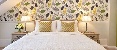 A bedroom with a large bed, two nightstands, and a floral wallpaper design.