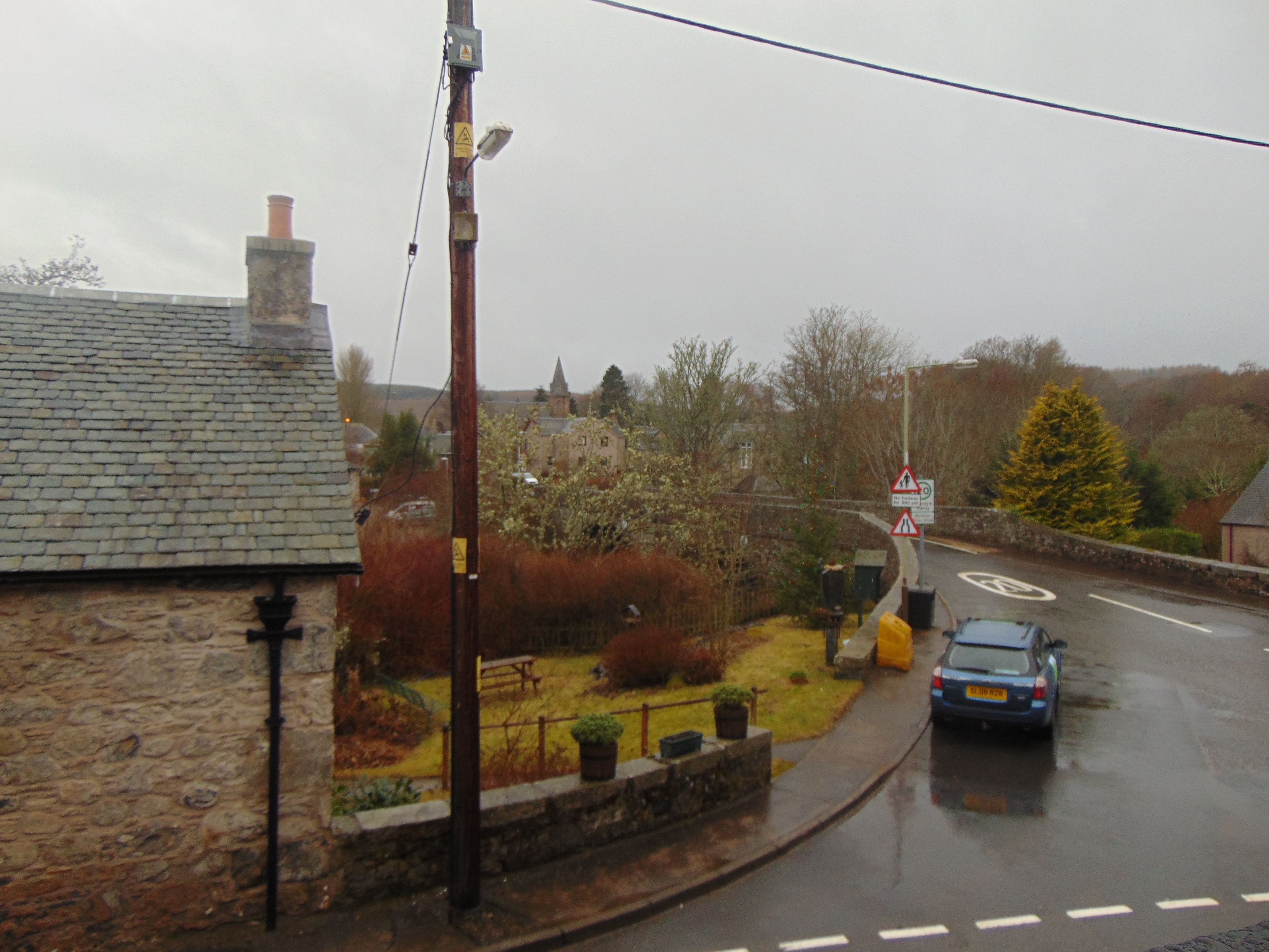 A rural road with a stone house, a church, and a car.