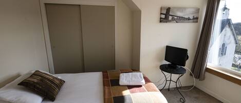 A hotel room with a bed, a television on a small table, and a window with a view of a building.
