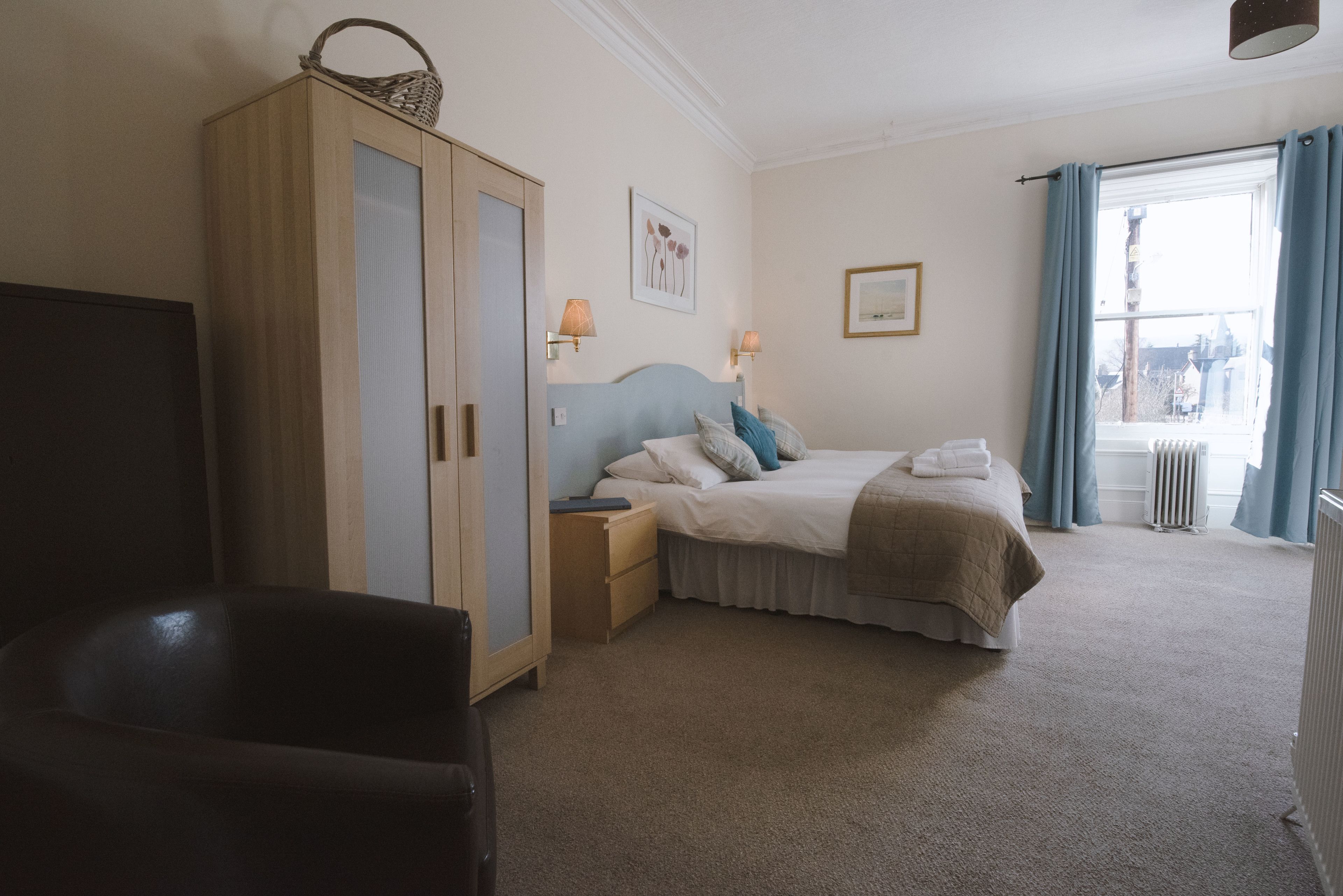 A bedroom with a bed, nightstands, a wardrobe, a chair, and a window with curtains.